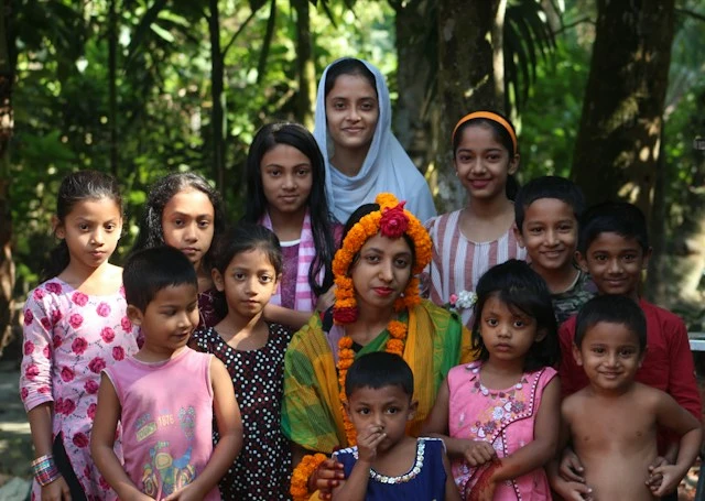 A group of children gathered around a woman wearing a flower garland outdoors.